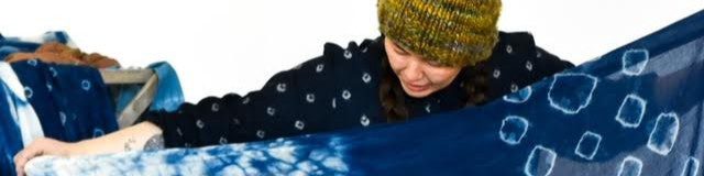 a person in a yellow hat looking down at an indigo dyed shawl, rich blue with white circles.
