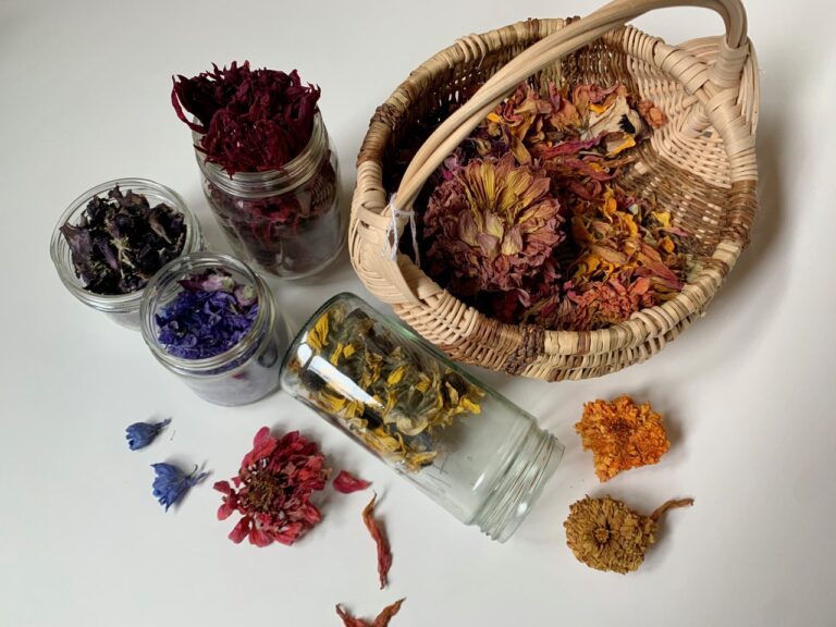 overhead view of dried colourful flower petals in mason jars and a woven basket on a white table