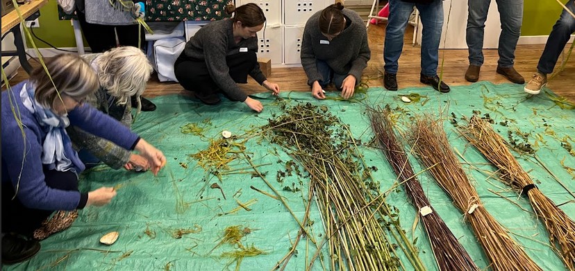 two people kneeling on the floor with a big pile of green nettle stalks