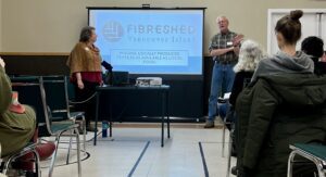 A woman and a man stand in front of a projector screen in a gymnasium.