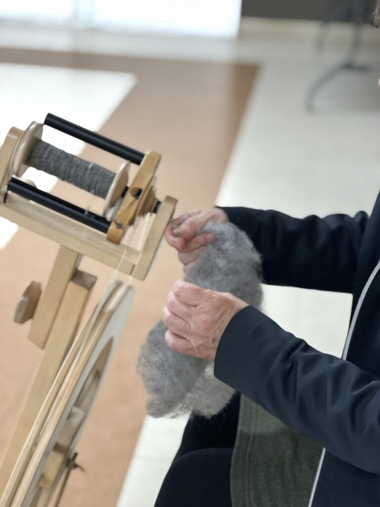 A person's hands holding grey wool carded roving at a Lendrum spinning wheel.