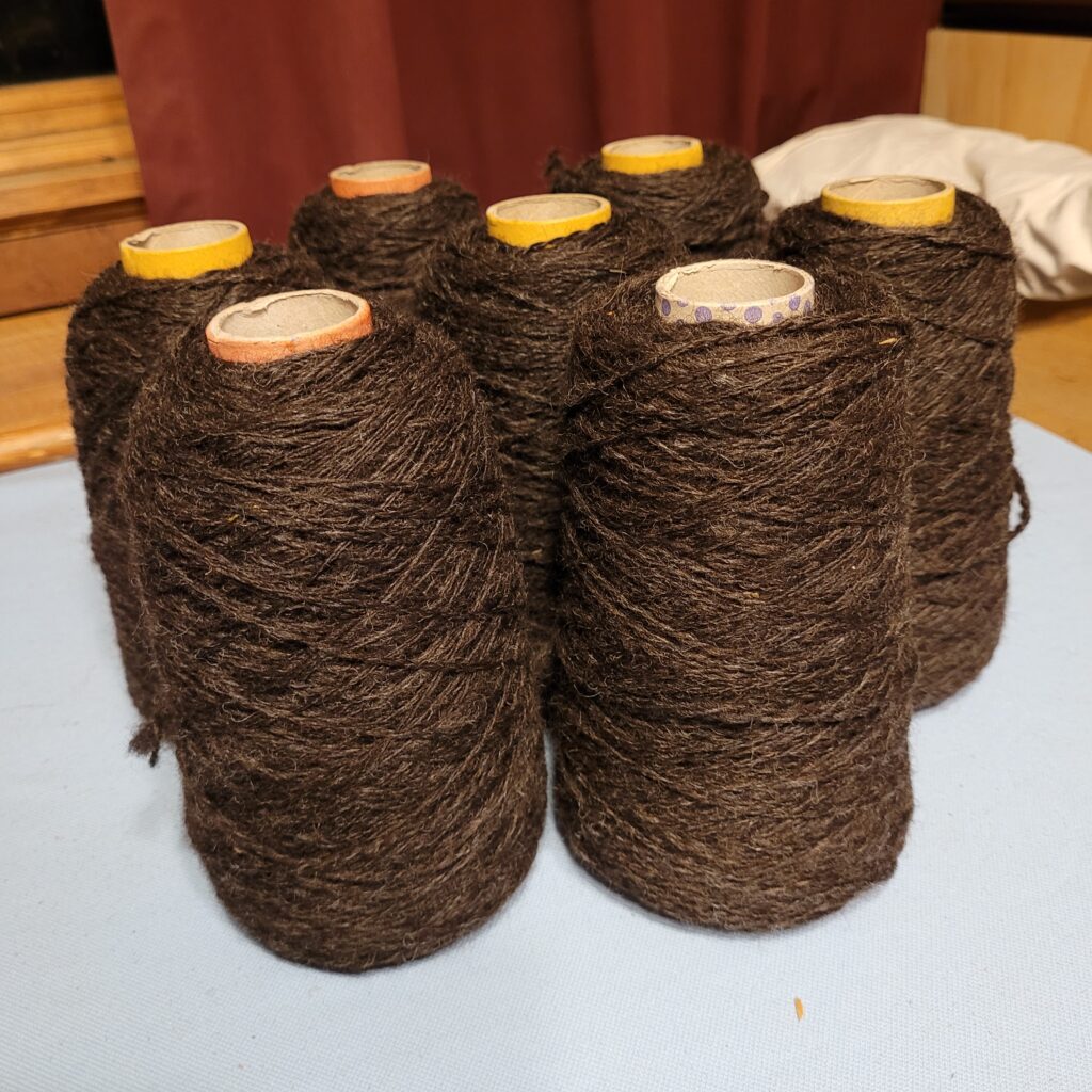 Cones of chocolate brown handspun 2ply yarn on a table. 