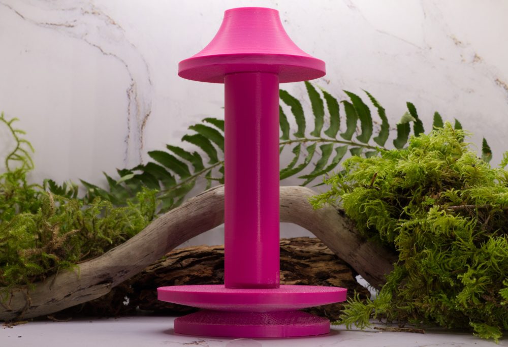 vibrant pink spinning wheel bobbin on a table with fern and moss behind