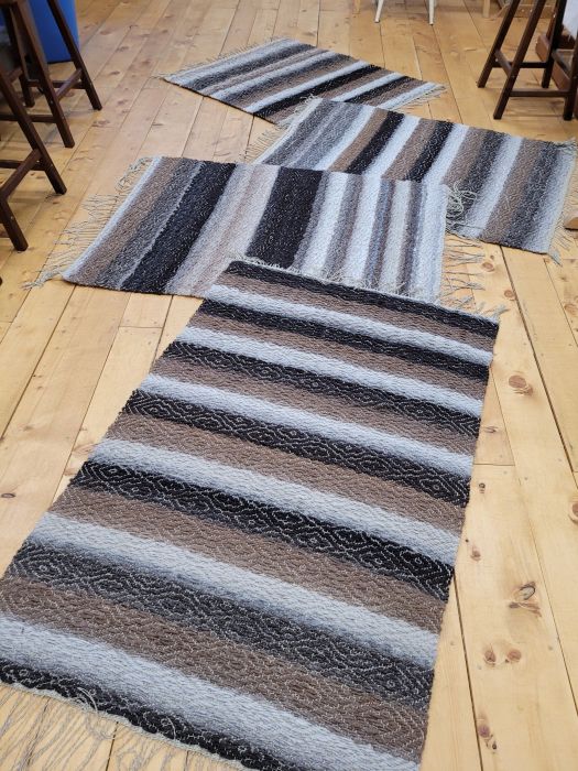 four woven rugs on a blond wood floor. Rugs are striped in natural alpaca colours (white, brown, grey)