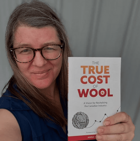 book being held by white woman with long brown hair and glasses looking at camera